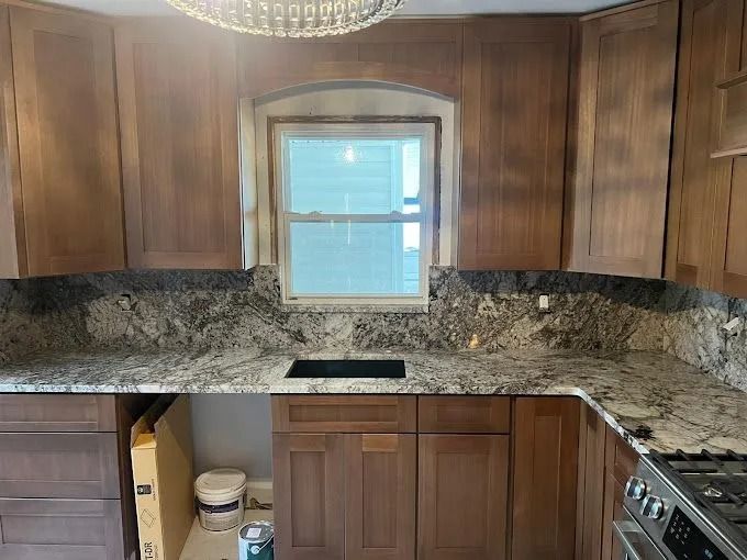 Kitchen with wood cabinets, granite countertops, centered window, and a sink under the window.