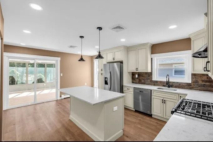Bright modern kitchen with white cabinets, stainless steel appliances, island, and large windowed dining area