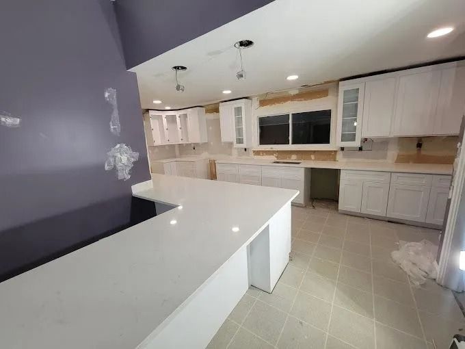 Bright modern kitchen with white cabinets, large island, tiled floor, and recessed ceiling lights