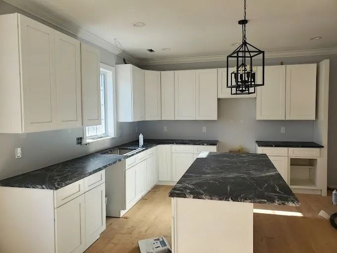 Bright kitchen with white cabinets, black countertops, and a central island under a pendant light.