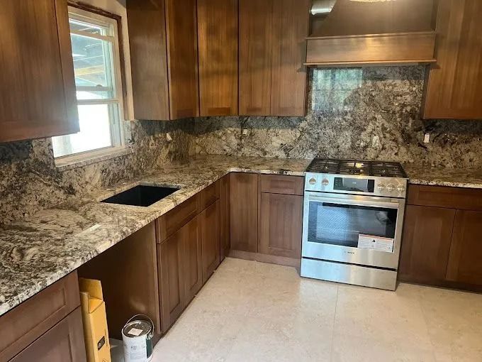 Small kitchen with brown cabinets, granite counters, stainless stove, and tiled backsplash.