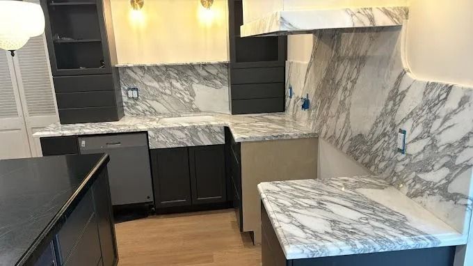 Modern kitchen with dark cabinets, marble-pattern counters and backsplash, and wood flooring
