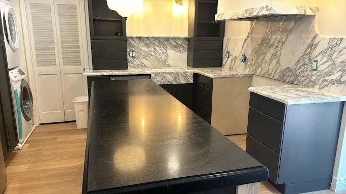 Modern kitchen with dark island countertop, marble backsplash, and black and white cabinetry