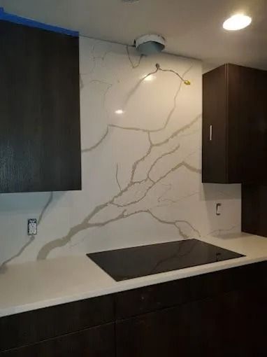 Modern kitchen with white marble-look backsplash, dark cabinets, and black cooktop.