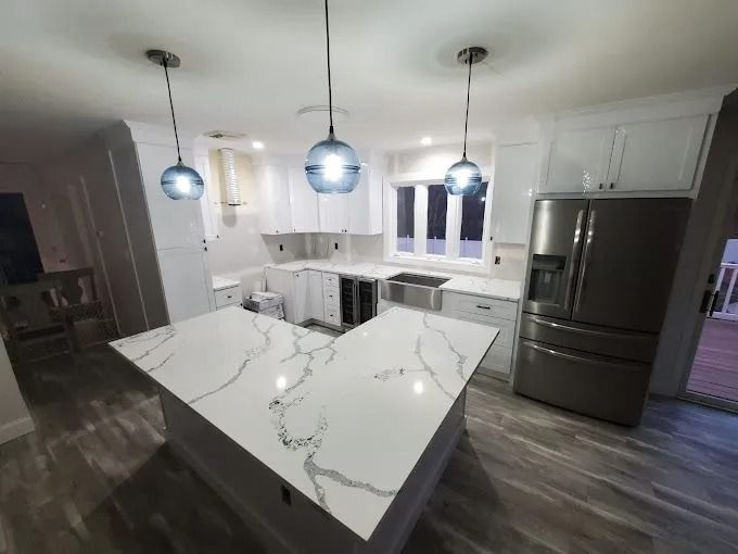 Modern white kitchen with marble island, pendant lights, dark wood floors, and stainless steel appliances