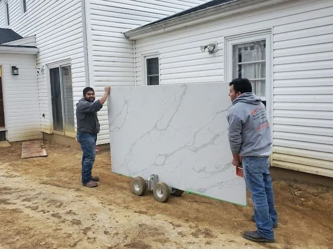 Two workers carry a large white marble slab beside a house under construction.