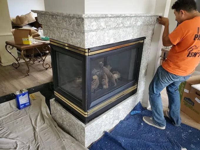 Corner fireplace installation in progress, with workers wrapping the base in blue protective covering.
