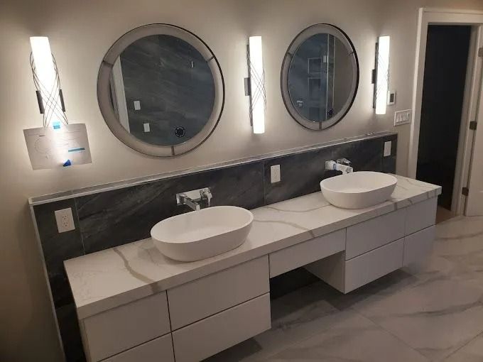 Modern bathroom vanity with two round mirrors, wall lights, and dual vessel sinks on a light countertop.