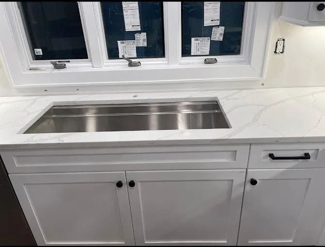 White kitchen sink cabinet with stainless steel undermount sink beneath a window