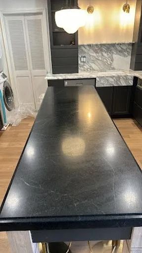 Kitchen with a long black island, dark cabinets, and white marble backsplash under warm lights