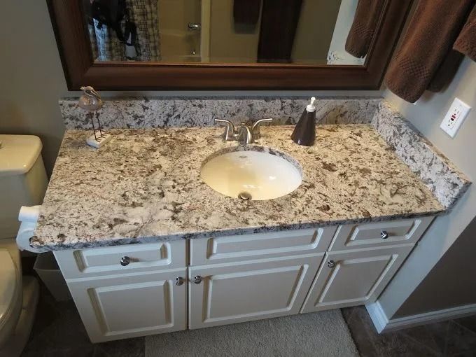 Bathroom vanity with speckled granite countertop, round sink, faucet, mirror, and brown hand towel￼