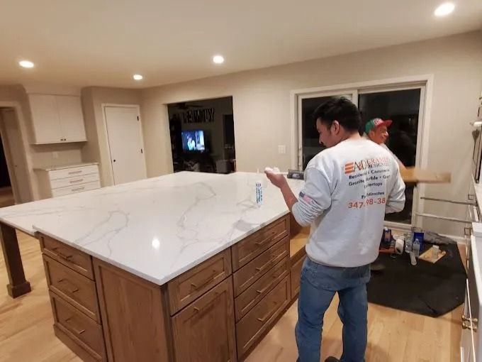 Two workers in a kitchen installing a large white marble island countertop