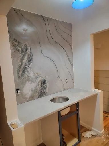 Bathroom vanity under construction with marble-look wall panel, sink cutout, and open cabinet frame
