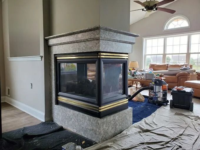 Living room with a large corner fireplace, high ceilings, and furniture covered during renovation