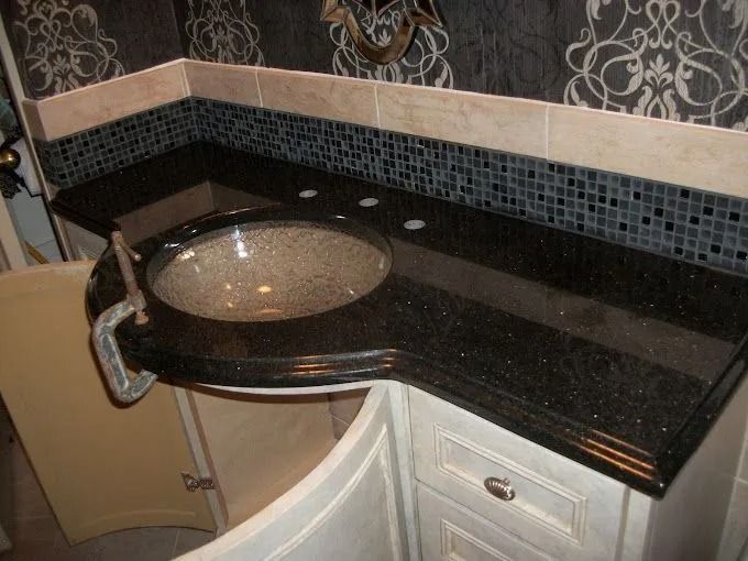 Black granite bathroom vanity with round vessel sink and mosaic tile backsplash