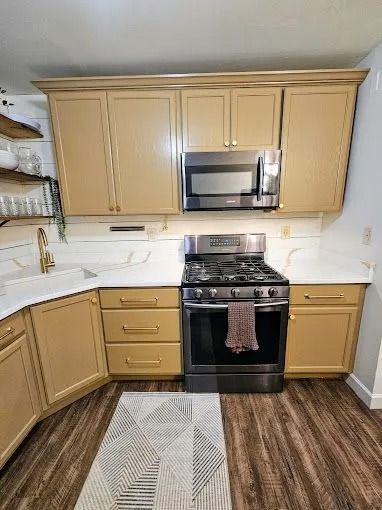 Kitchen with tan cabinets, stainless microwave and black stove, white backsplash, and wood-look flooring.