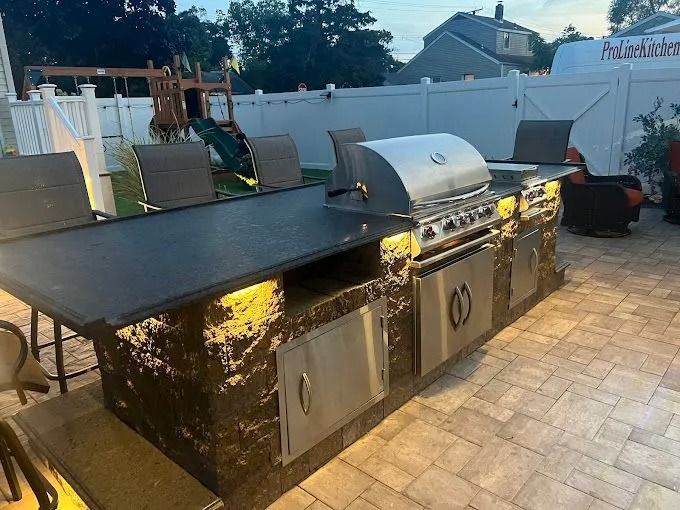 Outdoor backyard with a black granite grill island and stainless steel barbecue setup on a paved patio