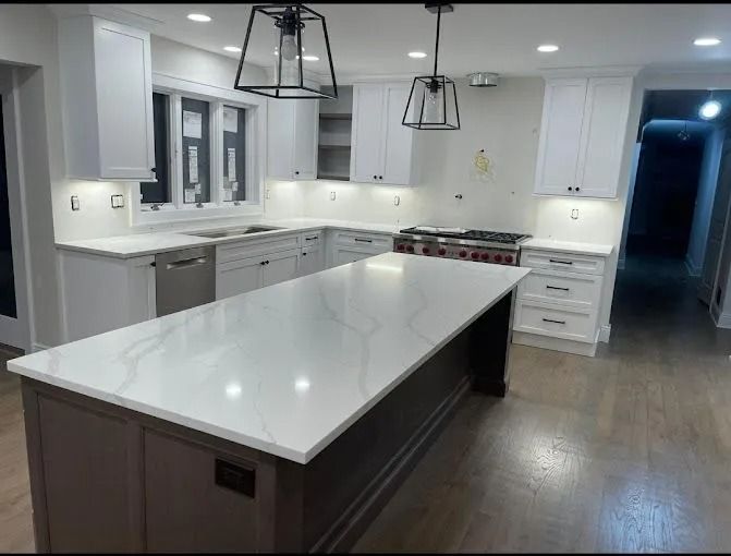 Modern white kitchen with large island, dark wood floor, pendant lights, and stainless appliances