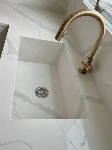 White stone sink with gold faucet in a marble-tiled bathroom.