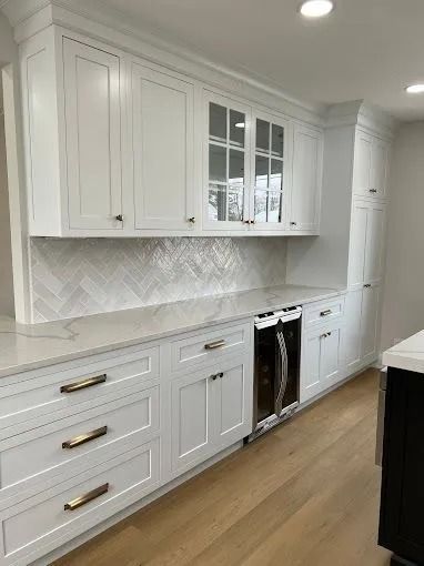 White kitchen with shaker cabinets, glass fronts, brass pulls, and light wood floors.