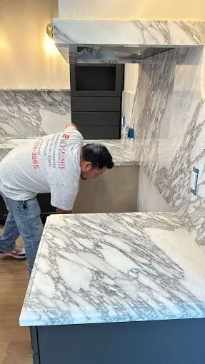 Person installing marble countertops in a kitchen with white and gray veining.
