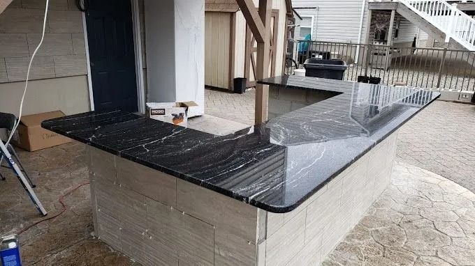 Black granite-topped outdoor bench or planter with beige stone base on a patio, beside steps and railing