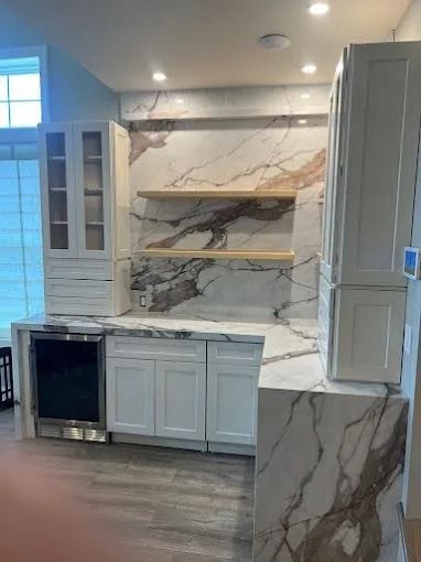 Modern kitchen with white cabinets, marble-look backsplash, open shelves, and a large island under construction