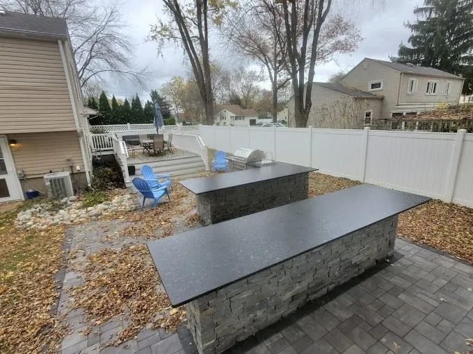 Backyard patio with two black stone tables and a white vinyl fence, covered in fallen leaves