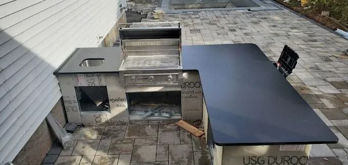 Outdoor patio with a built-in stainless steel grill and dark countertop beside a house