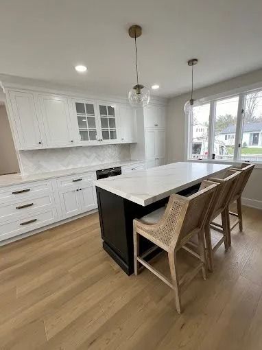 Bright modern kitchen with white cabinets, island, wicker stools, and large windows