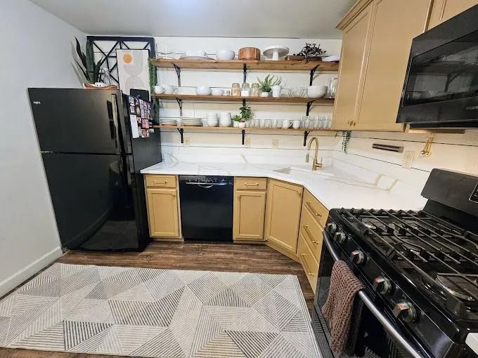 Modern kitchen with black appliances, light wood cabinets, open shelves, and patterned rug