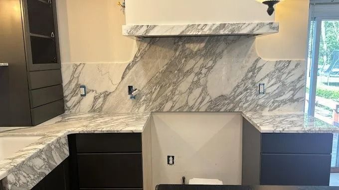 Modern kitchen with white marble countertops, dark cabinets, and a range hood over the cooktop area