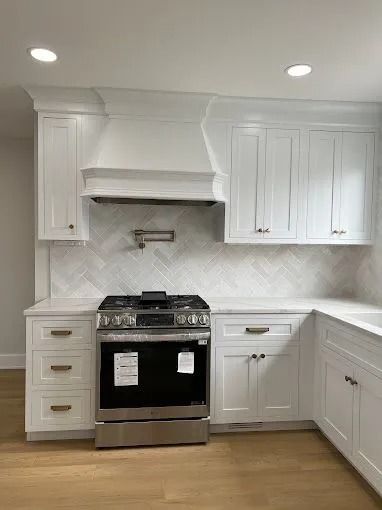 White kitchen with black stove, marble backsplash, and white cabinets under recessed lights