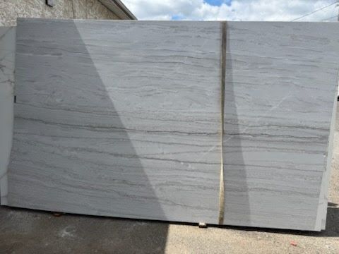 Stack of large white stone slabs secured with a strap outdoors against a building wall