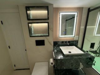 Modern bathroom vanity with lit mirror, sink, toilet paper holder, and shower door in view
