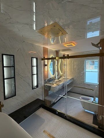 Modern bathroom with walk-in shower, glass partition, marble walls, and skylight.