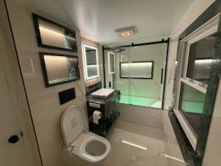 Modern bathroom with toilet, vanity, large windows, and green-lit shower area