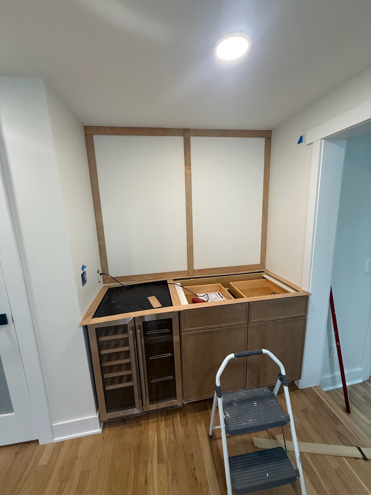 Partially renovated kitchen with unfinished cabinets, countertop materials, and a step ladder on the floor