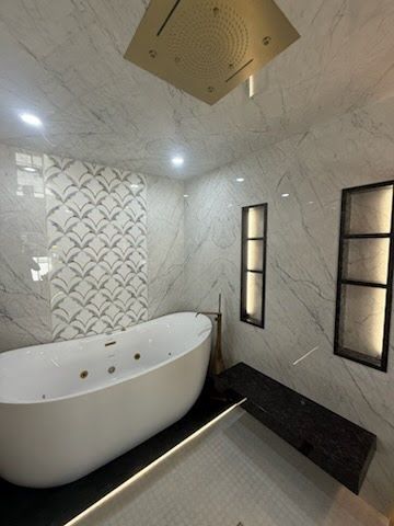 Modern bathroom with a freestanding white tub, marble walls, walk-in shower, and black accent trim