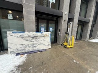 Marble slab leaning outside a gray building entrance beside a yellow pallet jack on wet pavement