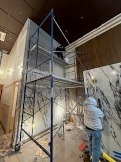 Workers on scaffolding installing a large wall-mounted display in a lobby with marble walls