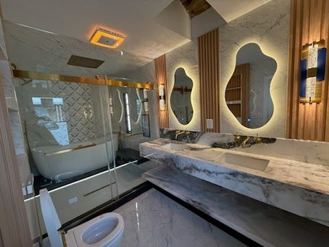 Modern bathroom with marble vanity, oval mirrors, bathtub, glass shower, and warm ceiling lights