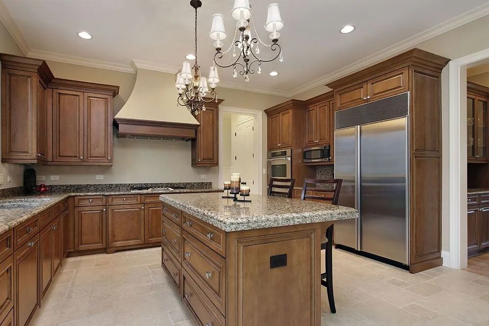 Spacious kitchen with dark wood cabinets, granite island, stainless steel refrigerator, and chandelier lighting