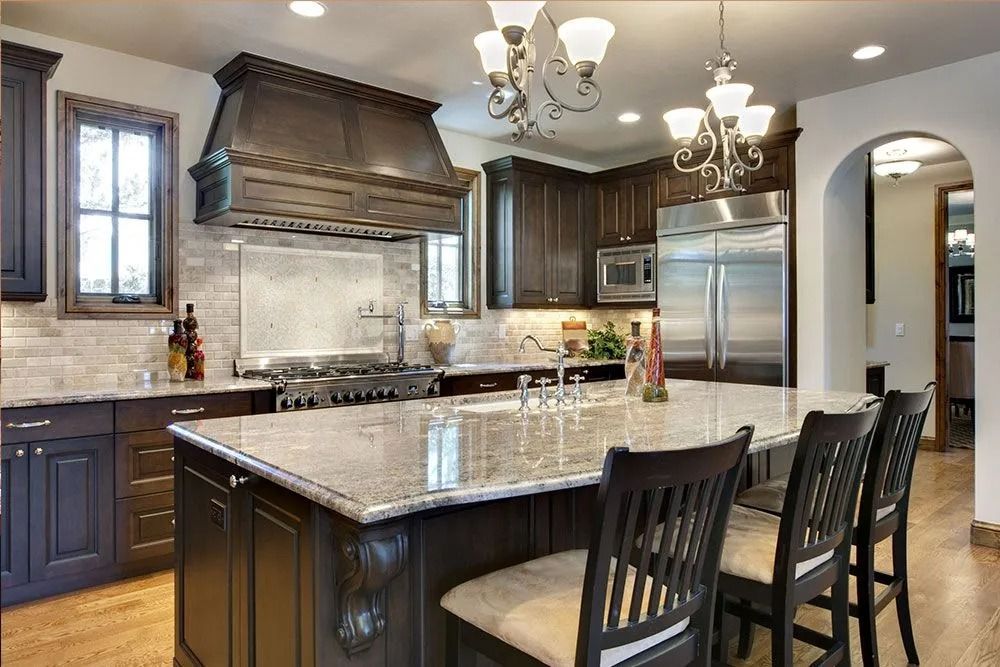 Modern kitchen with dark cabinets, granite island, stainless steel appliances, and bar stools