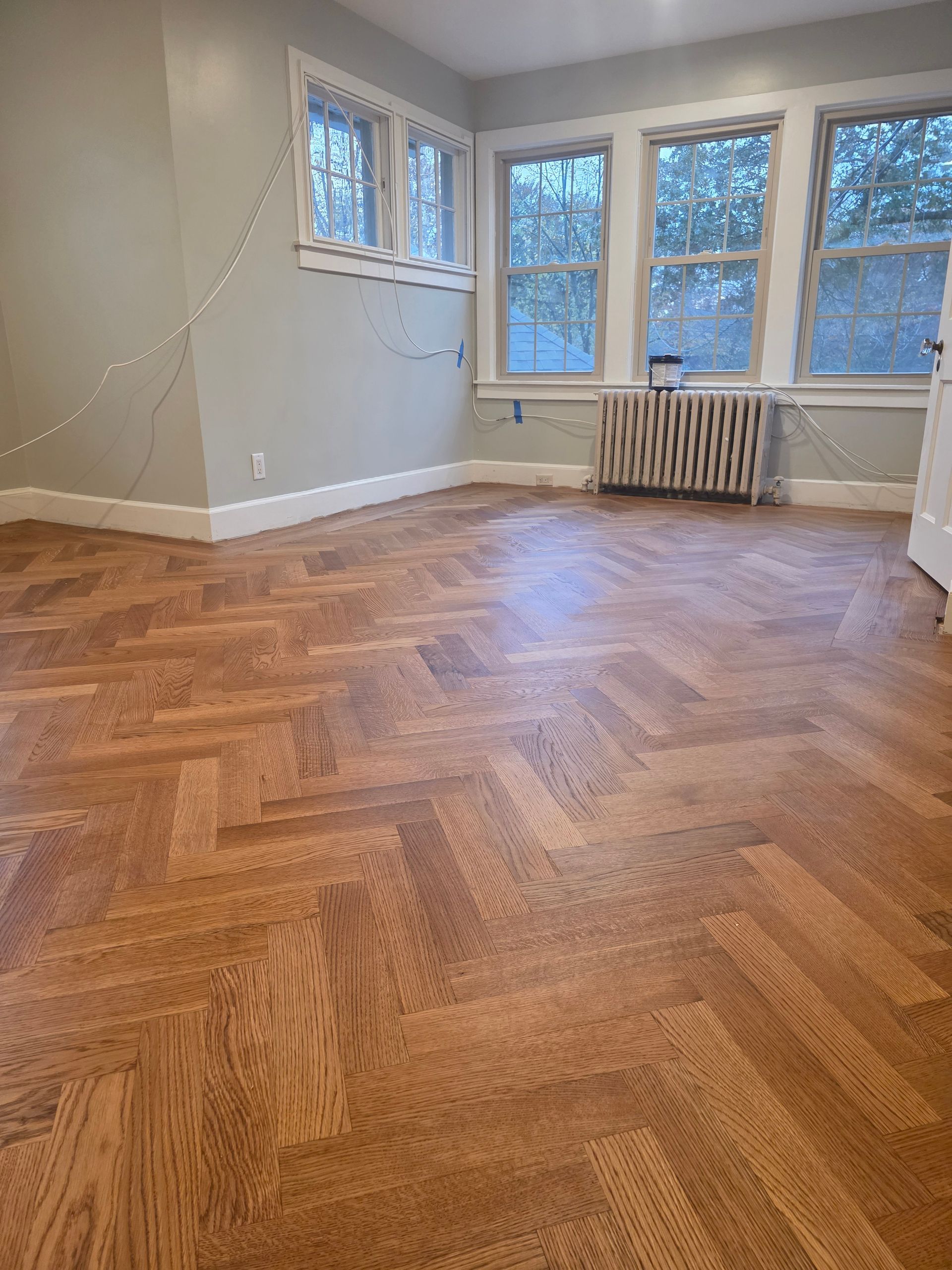 Room with hardwood parquet flooring, light blue walls, and multiple windows.