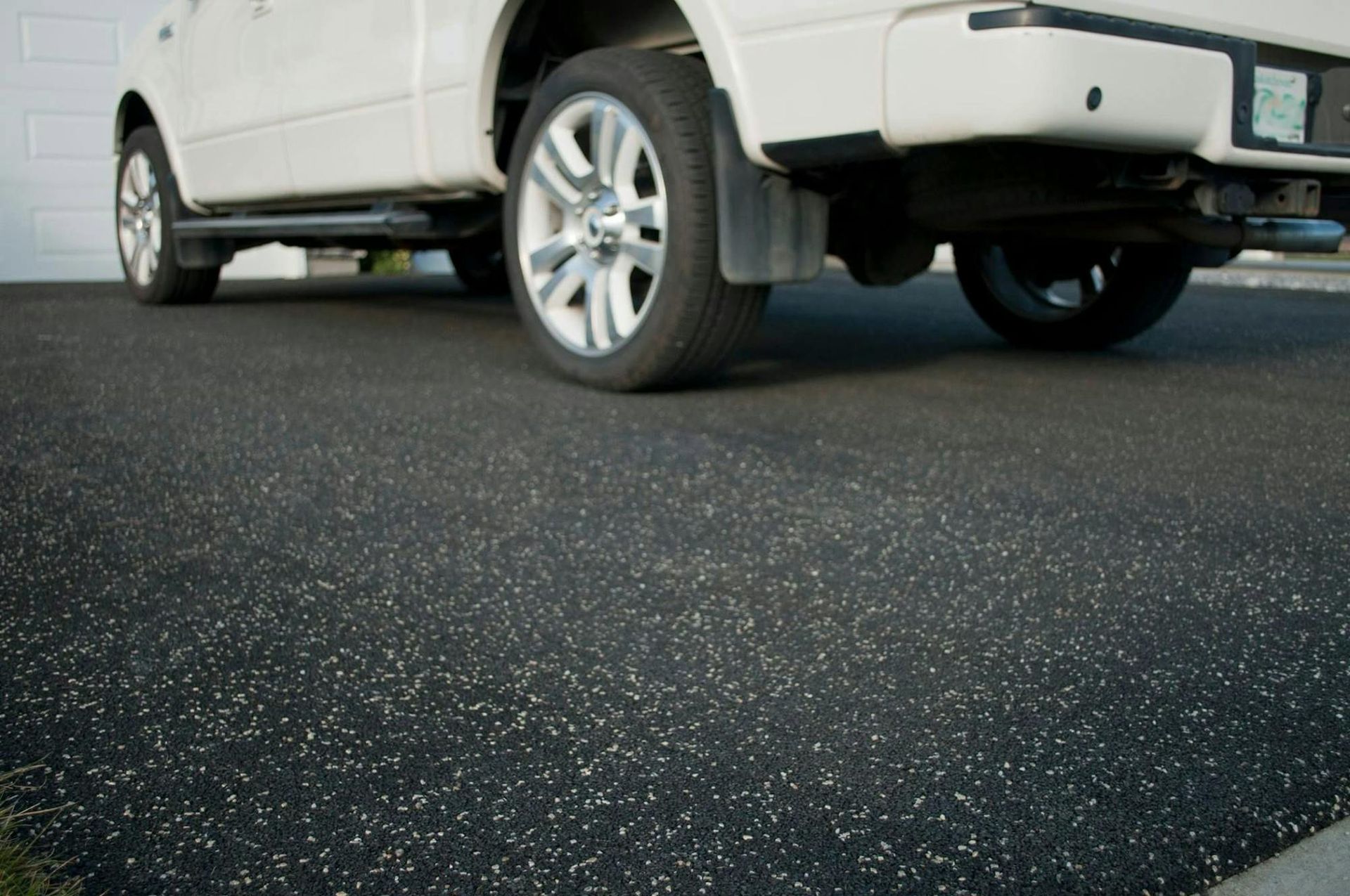 A white truck is parked on a black asphalt driveway.
