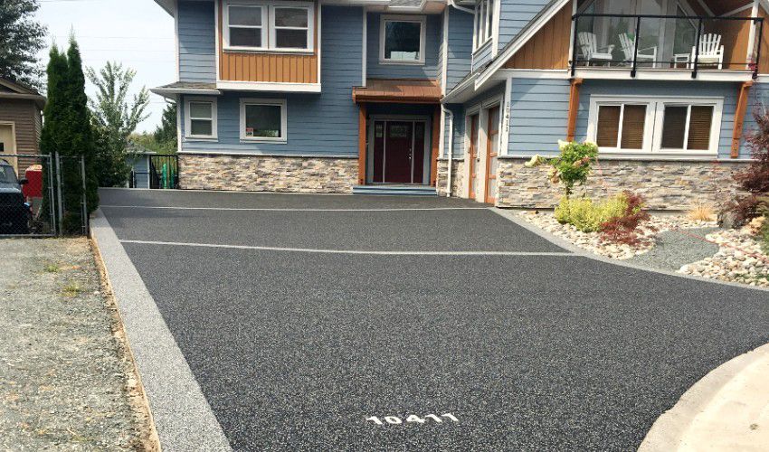 A large blue house with a black driveway in front of it.