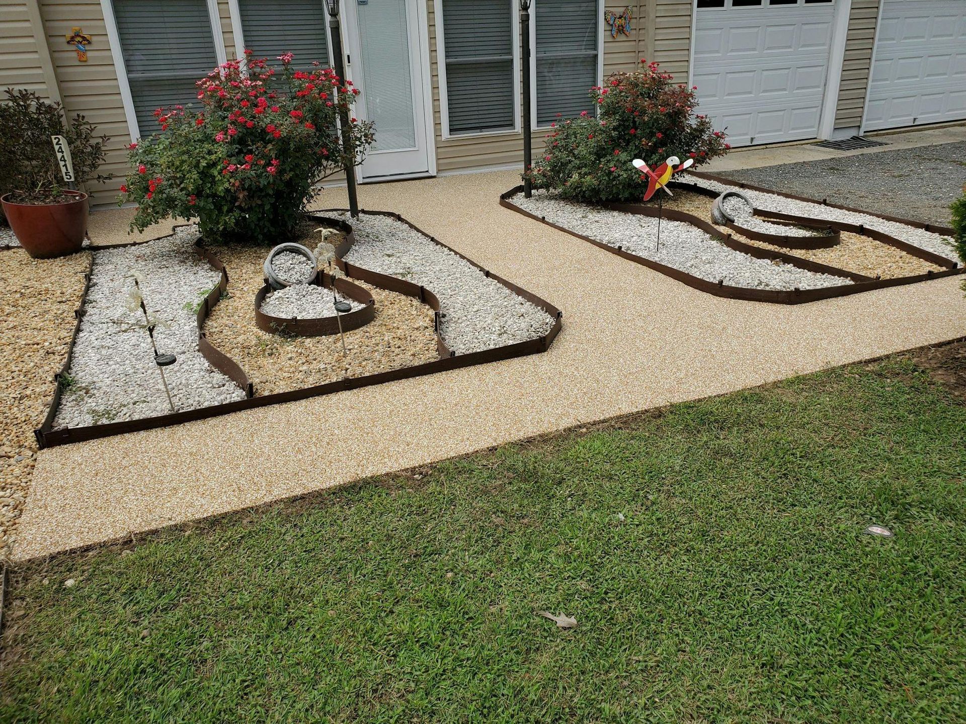A walkway with gravel and flowers in front of a house.