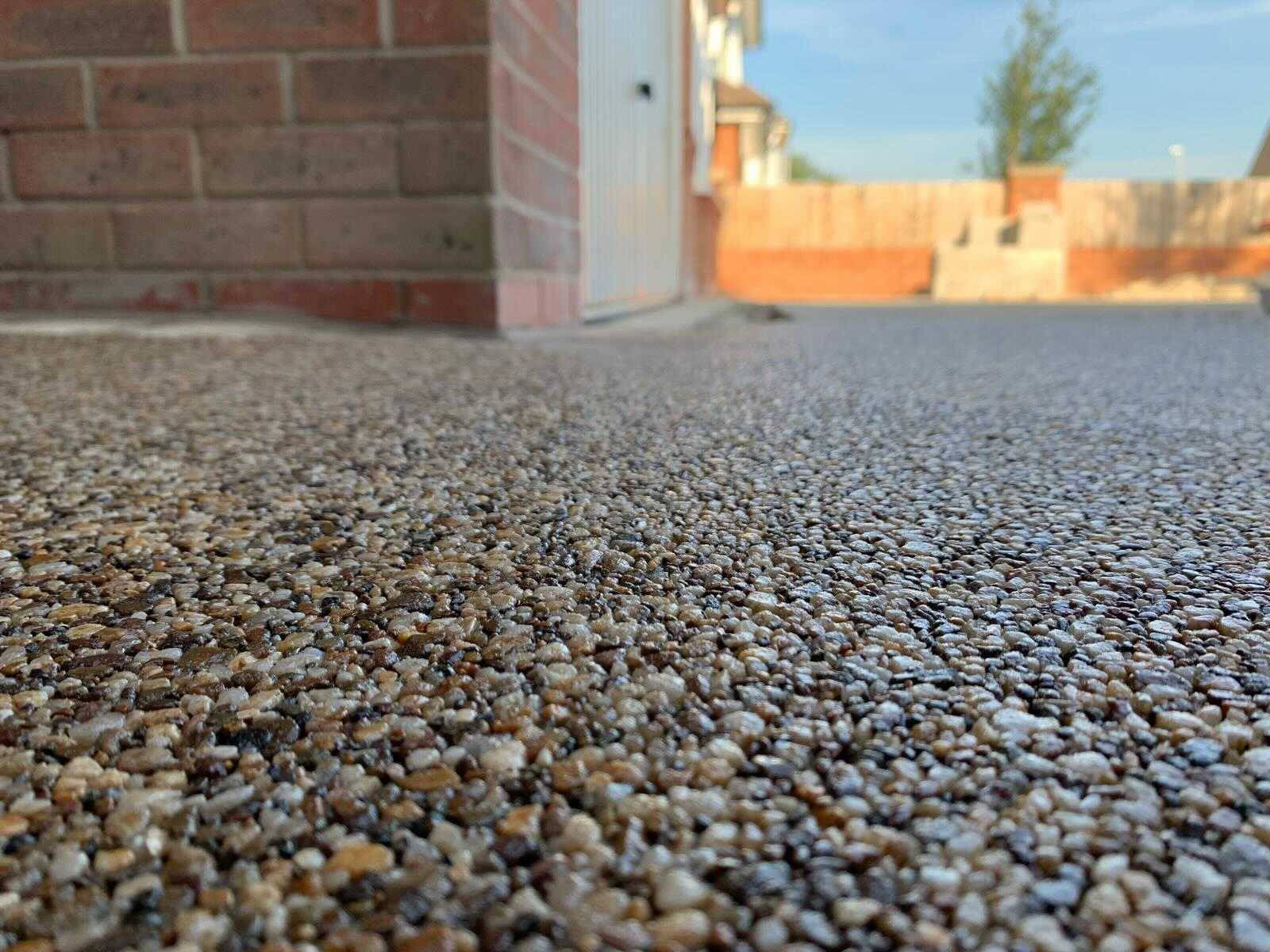 A close up of a gravel driveway with a brick wall in the background.