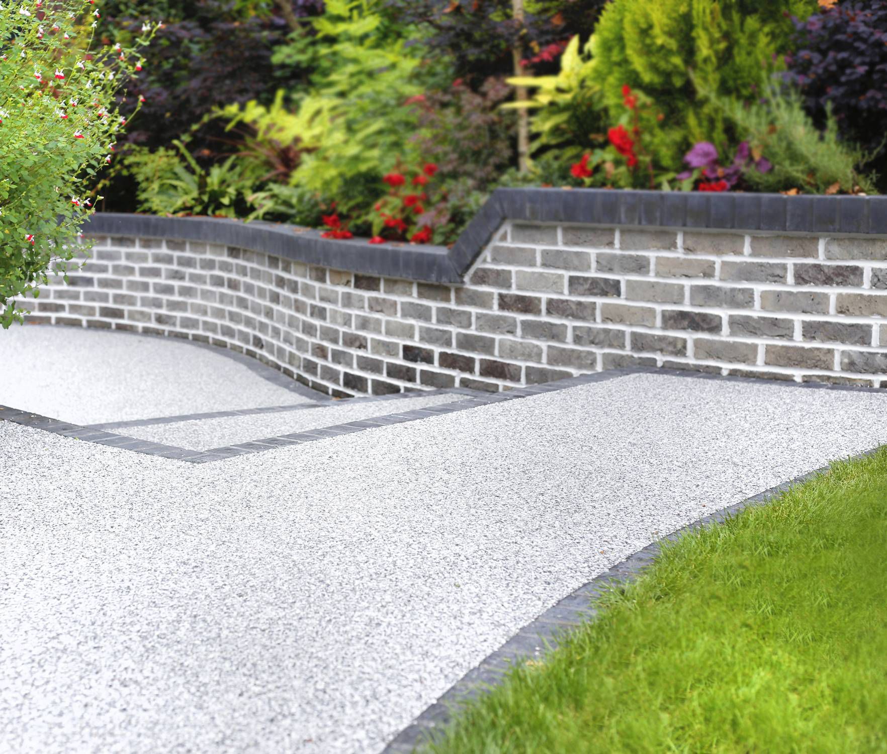 A brick wall surrounds a gravel path in a garden.